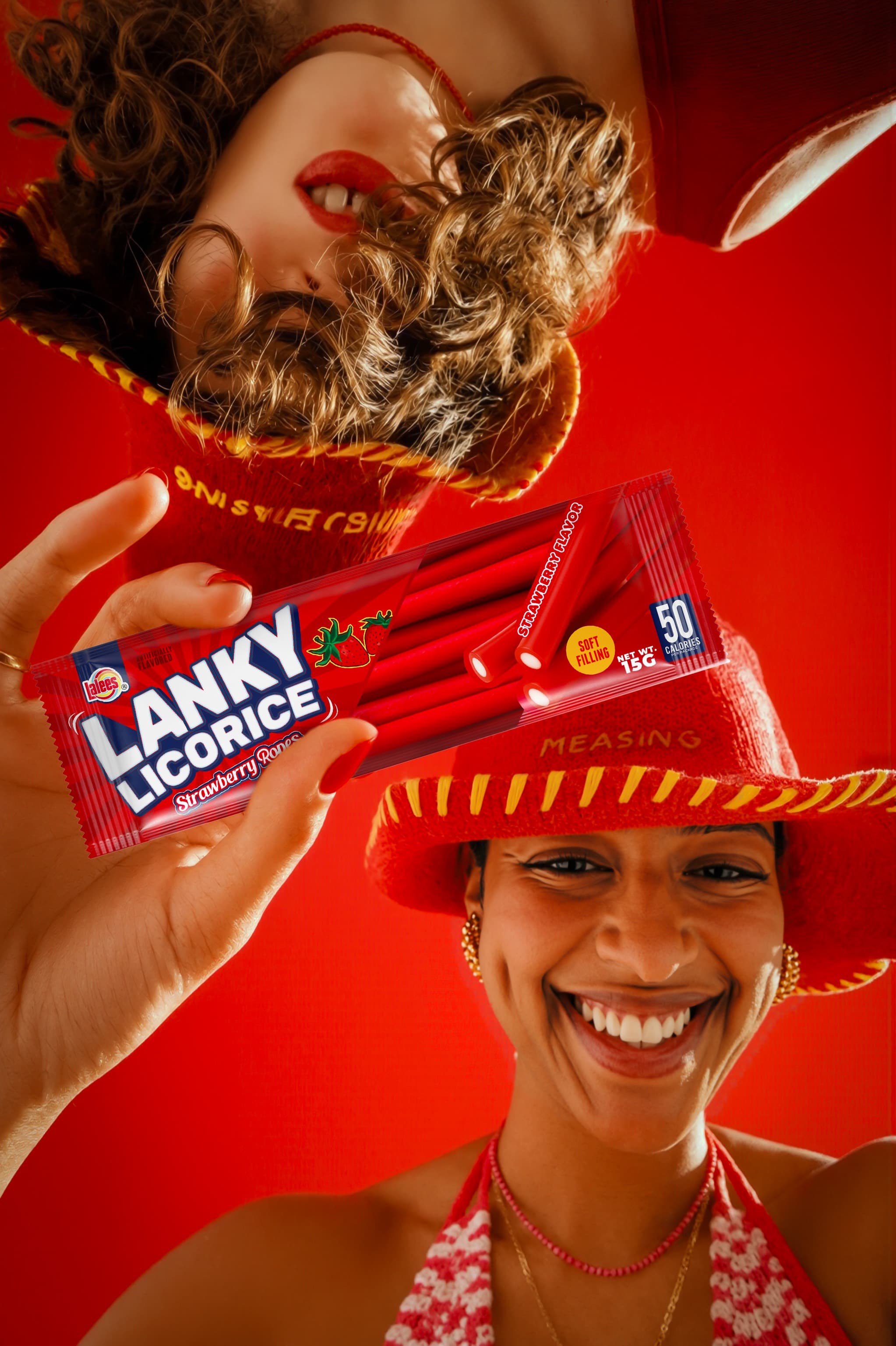 Smiling woman in a straw hat holding a Lanky Licorice stick pack toward the camera against a red backdrop