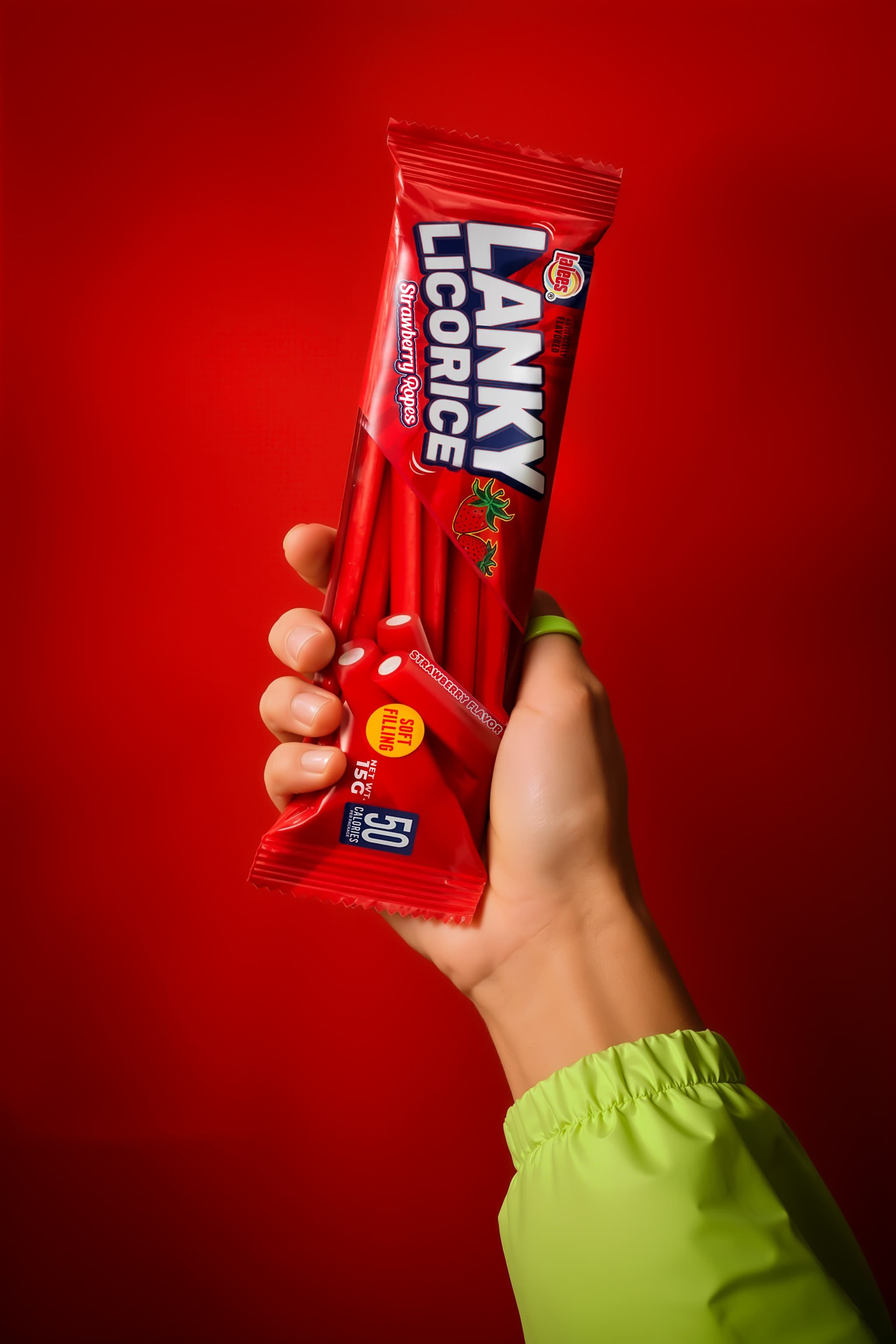 Hand in a green sleeve holding a single stick pack against a red background