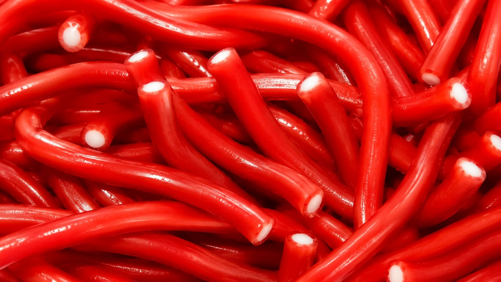 Macro photograph of glossy red licorice ropes with soft white filling visible at the cut ends