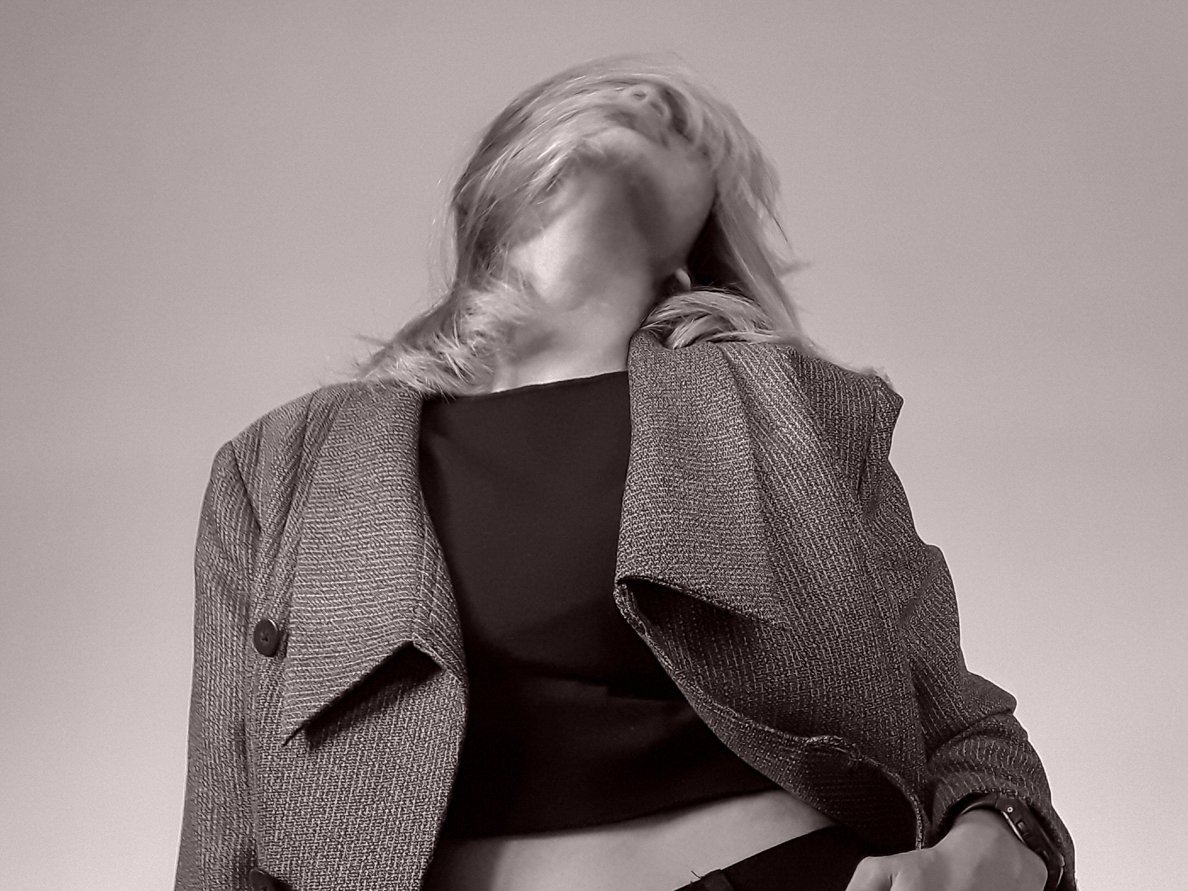 Blurred editorial fashion figure in a tweed jacket against a soft blush backdrop — mood for the Greatness identity