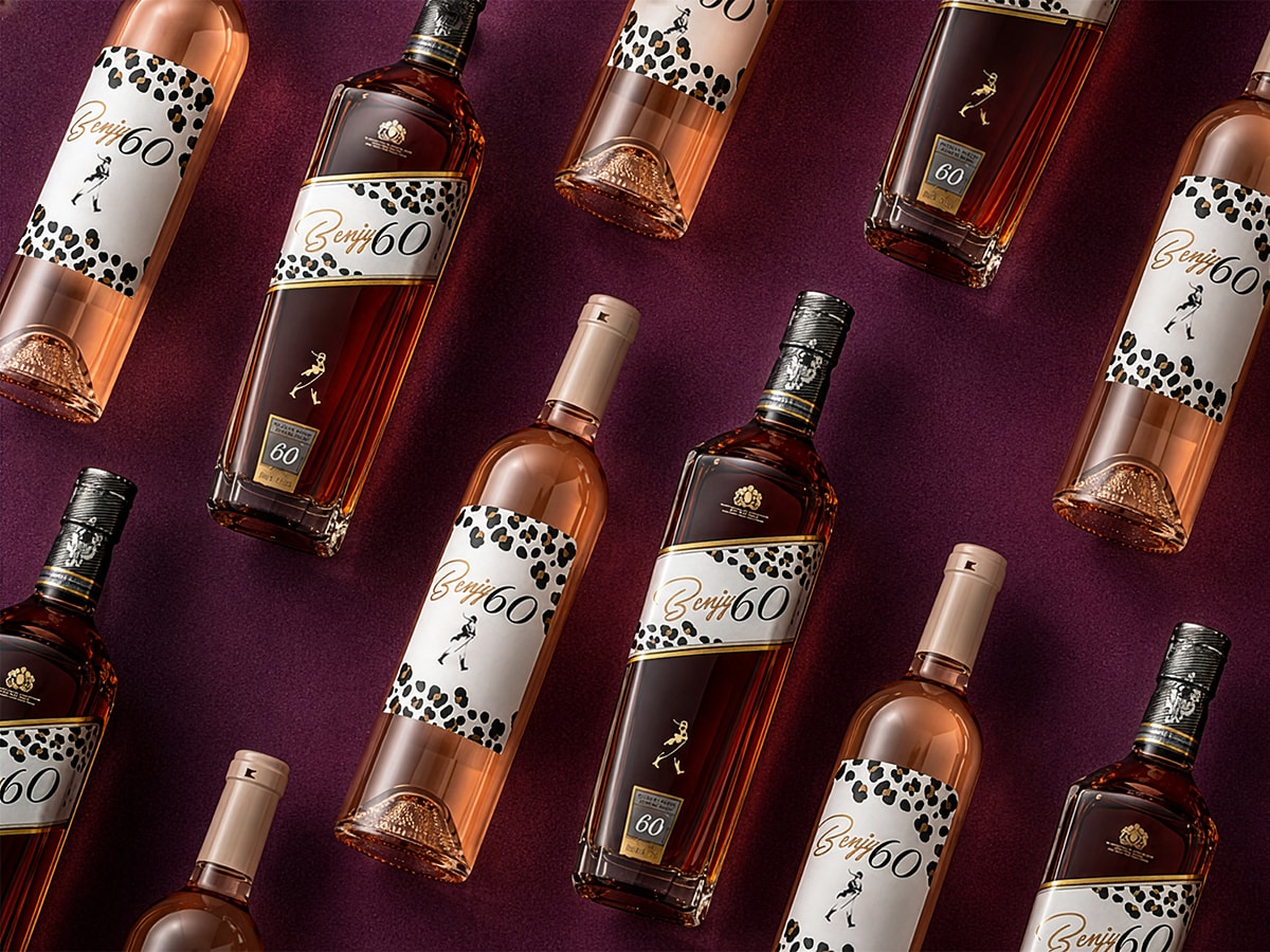 Overhead flat-lay of Benjy60 whiskey and rosé bottles arranged on a deep maroon surface