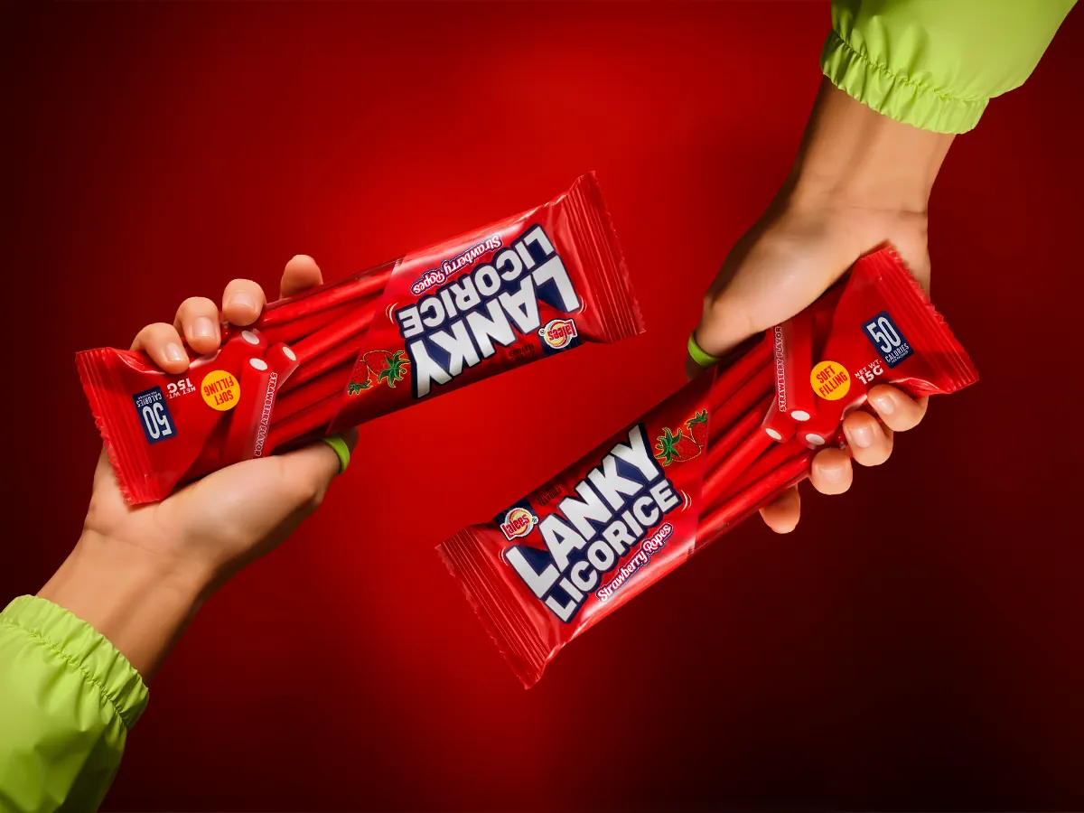 Two hands passing Lanky Licorice strawberry rope packs against a red background